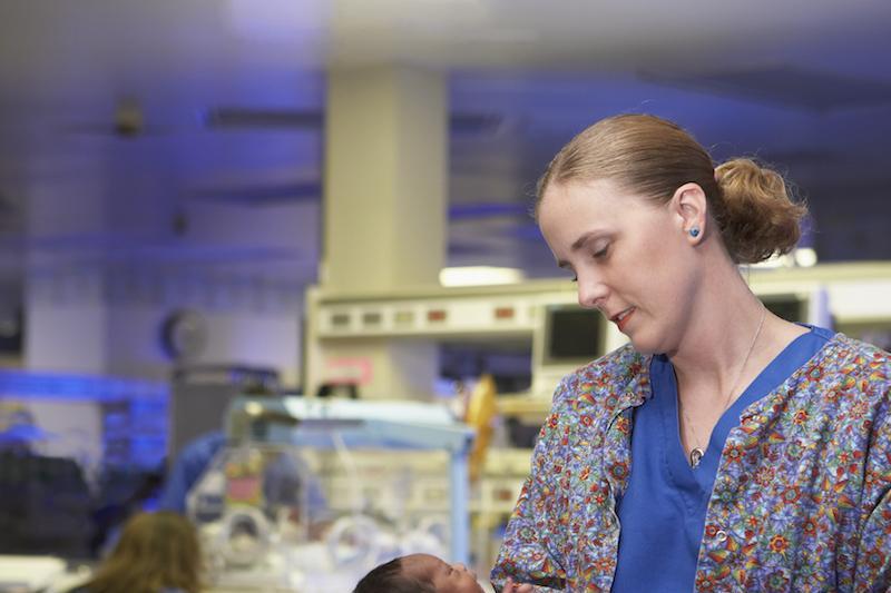 A healthcare worker carrying a newborn baby in neonatal intensive care unit